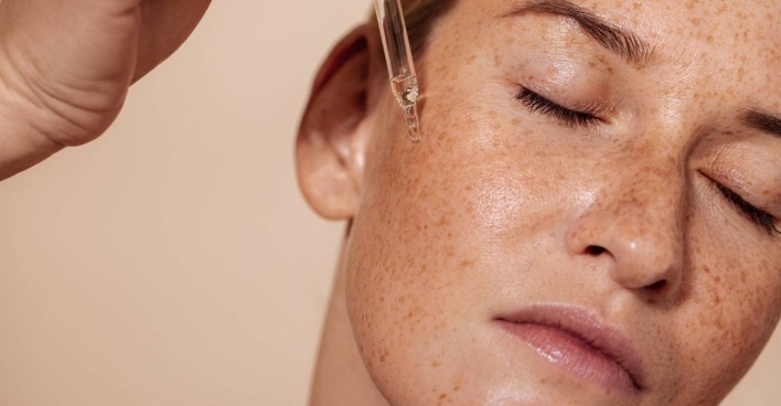 Junge Frau beim Auftragen eines Serums aus einer Ampulle auf die Haut