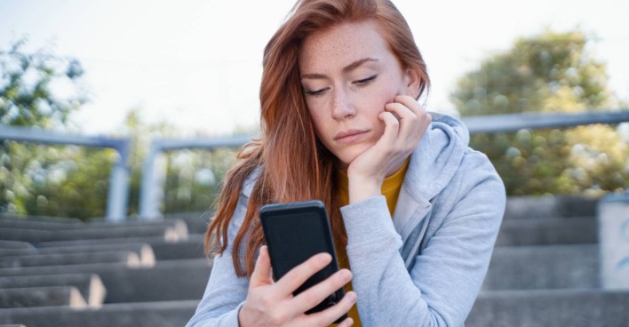 Junge Frau, die traurig auf das Display ihres Smartphones schaut.