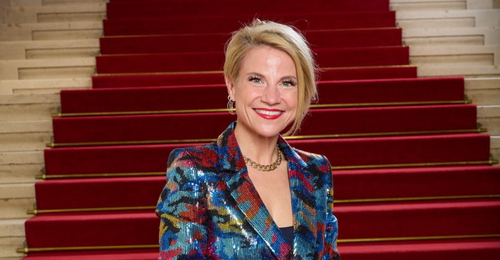 Kristina Sprenger vor einem Treppenaufgang mit einem bunten Anzug.