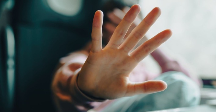 Ein Mädchen signalisiet mit einer ausgestreckten Hand "Stopp". Die andere hat sie verzweifelt über ihr Gesicht gelg.