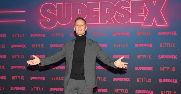 Rocco Siffredi in einem Anzug vor einer Fotowand vom Netflix Film "Supersex"