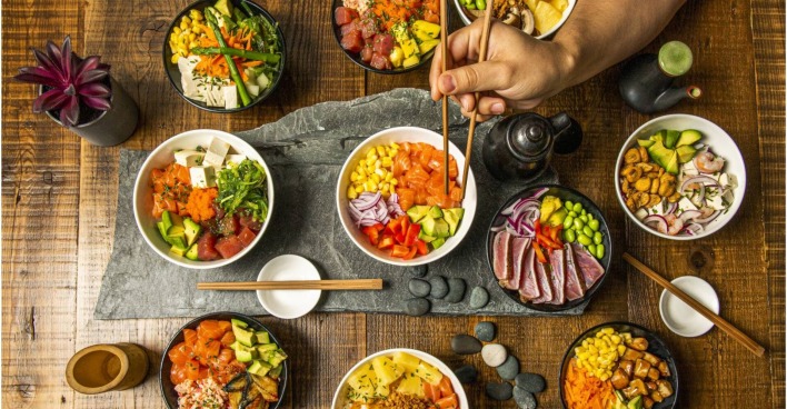 Vogelperspektive auf einen Tisch mit 7 verschiedenen Sushi Bowls.