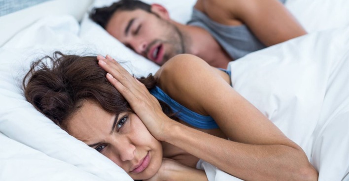 Junge Frau, die wach neben ihrem Partner im Bett liegt und sich die Ohren zuhält