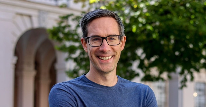 Kay-Michael Dankl im porträt. Er steht lachend im Freien und schaut direkt in die Kamera