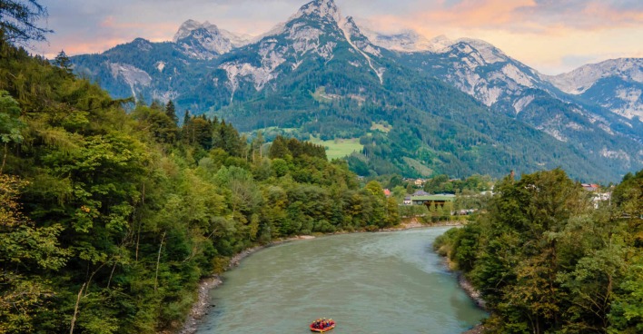 Eien Rafting-Gruppe auf einem Fluss, umgeben von Wald mit einem Blick auf österreichische Alpen.