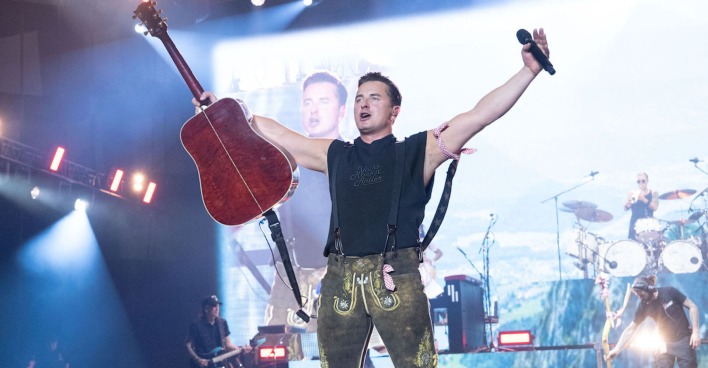Andreas Gabalier auf der Bühne mit einer Lederhose und einer Gitarre.