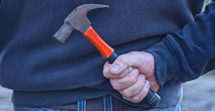 Ein Mann hält einen Hammer versteckt hinter seinem Rücken.
