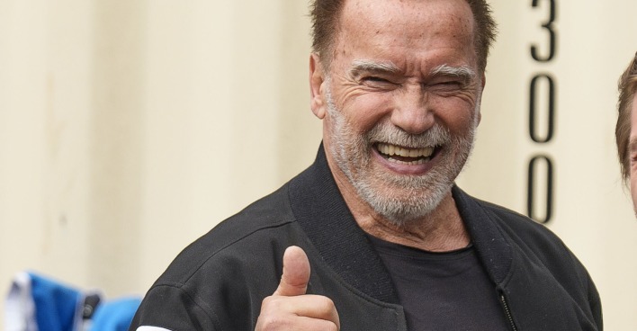 Arnold Schwarzenegger hält seinen Daumen hoch und lacht.