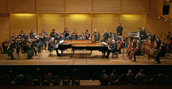 Orchester mit Pianisten, Chello- und Geigenspieler vor einem Publikum