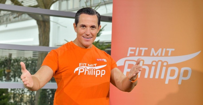 Philipp Jelinek in seine Fitness-Dress vor einem Banner mit der Aufschrift "Fit mit Philipp"
