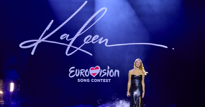 Kaleen auf der Bühne. Dahinter steht "Eurovision Song Contest". Sie trägt ein langes, schwarzes Ballkleid.