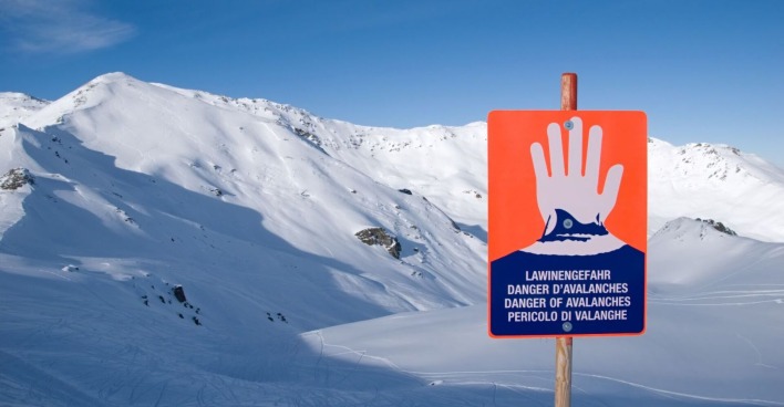 Hinweisschild für Lawinengefahr vor verschneiten Bergen.
