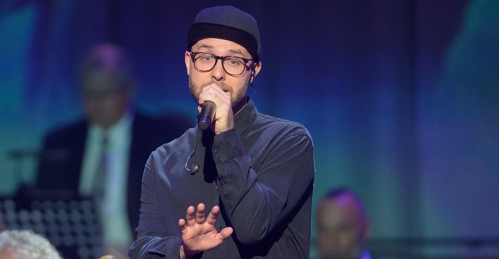 Mark Forster auf der Bühne mit einem Mikrofon und einer Kappe.