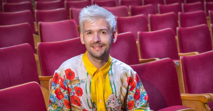 Michi Buchinger mit einem bunten T-Shirt auf einer Sitzreihe.