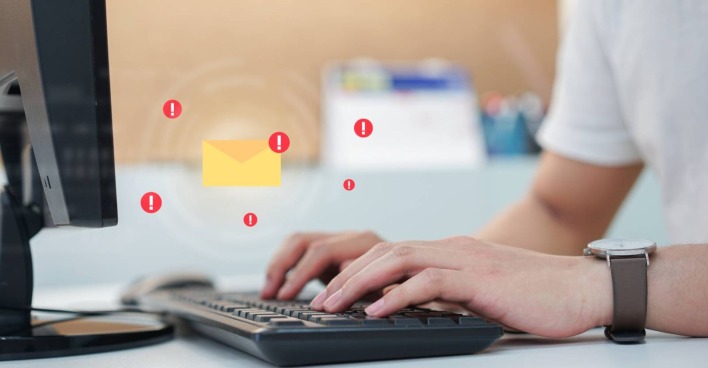 Ein Symbolbild für einen Phishing-Versuch. Illustriertes Briefsymbol über der Tastatur einer Person, die gerade etwas am PC bearbeitet.