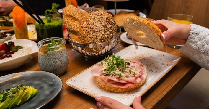 Reich gedeckter Frühstückstisch mit einem Bagel mit Schinken, frischem Meerrettich und Kräutern.