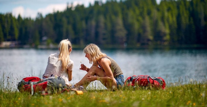 2 junge Frauen, die beim Ufer eines Sees sitzen