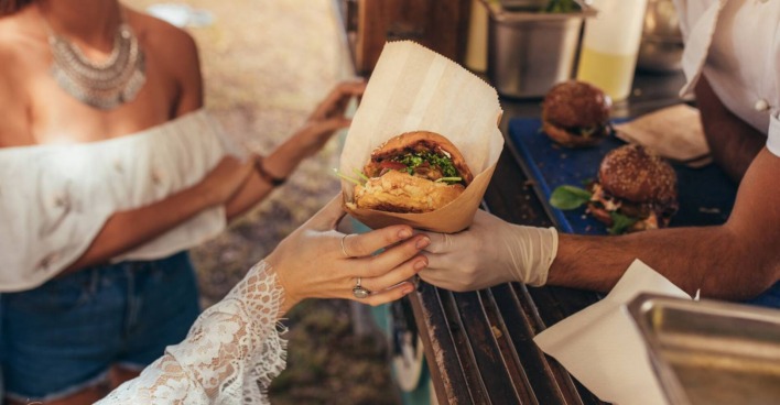 Frauenhand greift bei einem Foodtruck nach einem Burger.