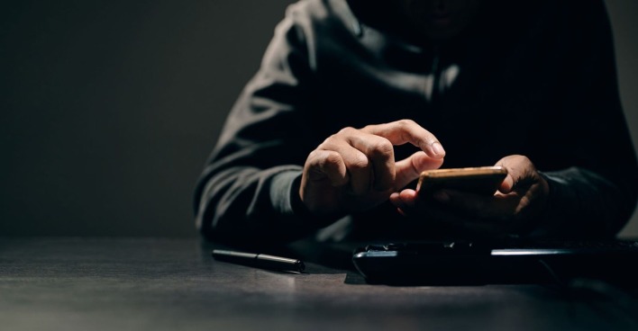 Ein Bursche tippt in Dunkeln etwas in sein Smartphone.