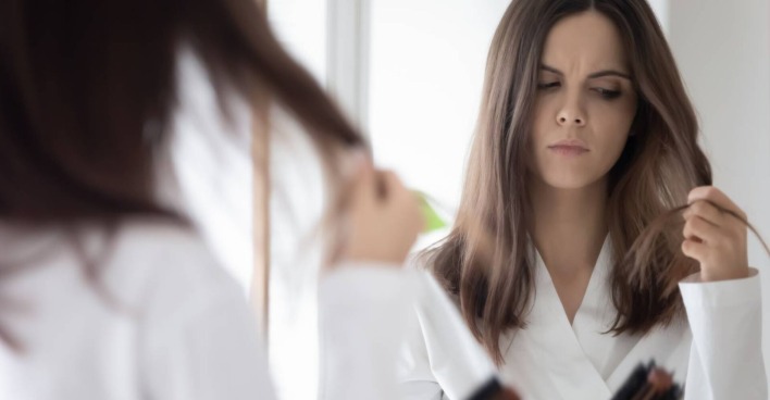 Besorgte junge Frau, die sich über die Dichte ihres Haares Gedanken macht, weil sie Haarausfall vermutet.