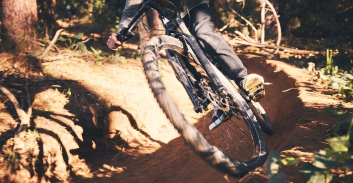 Ein Downhill-Biker fährt über eine Trail im Wald hinunter.