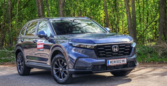 Ein blauer Honda CR-V strahlt in der Sonne. Im Hintergrund sind Laubbäume zu sehen, die ebenfalls in der Sonne leuchten.