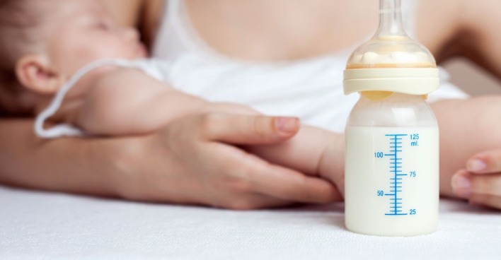 Eine Mutter hält ihr Baby, davor steht das Fläschchen.