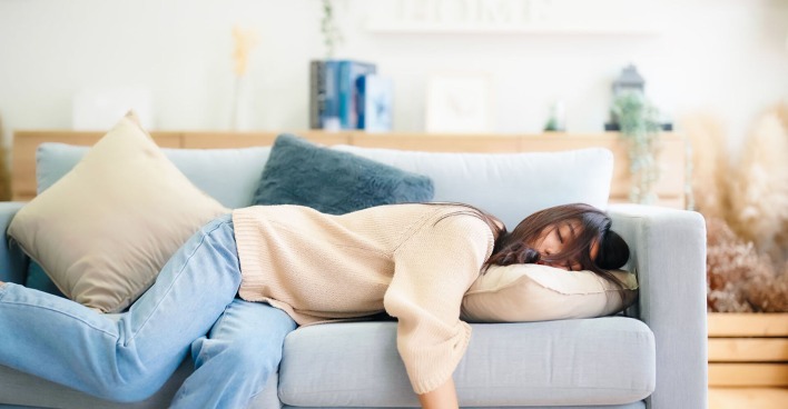 Frau liegt erschöpft auf einem Sofa | Credit: iStock.com/marchmeena29