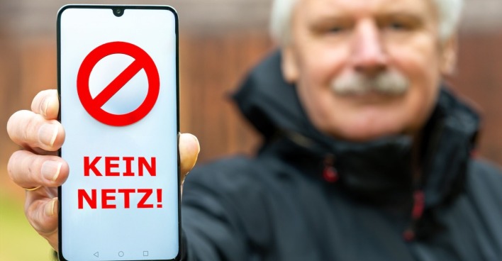 Eine Mann hält eine Handy mit einer "Kein Netz"-Aufschrift in die Kamera.