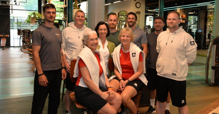 Mehrere Männer und Frauen posieren für ein Gruppenfoto in einem Fitnessstudio
