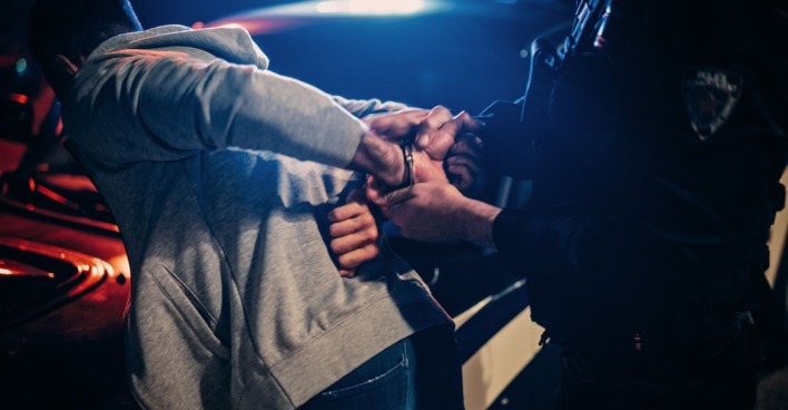 Ein Mann wird von einem Polizisten mit Handschellen festgenommen.