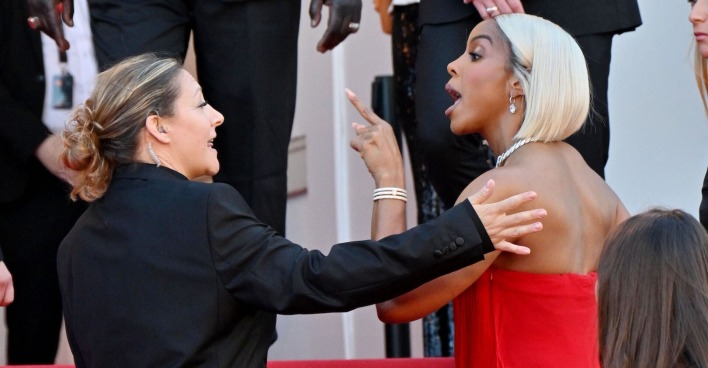 Kelly Rowland auf dem roten Teppich. Sie trägt blonde Haare und ein rotes Kleid und streitet mit dem sicherheitspersonal.