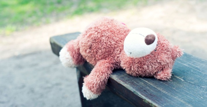 Ein einsamer Teddybär liegt auf einer Bank.