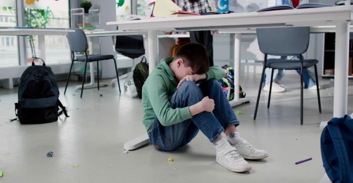 Ein Bub sitzt weinend auf dem Boden im Klassenzimmer.