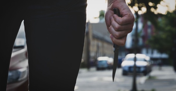 Ein Mann steht in einer Straße und hält ein Messer in der Hand.