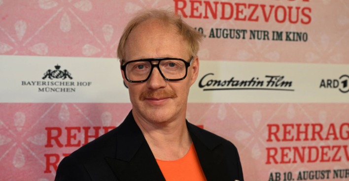 Simon Schwarz mit einem schwarzen Sakko und einem orangenen Hemd.