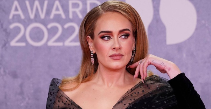 Adele mit starken Make Up und offenen Haaren bei einem Event. Sie schwingt mit ihrer Hand ihre Haare zurück.