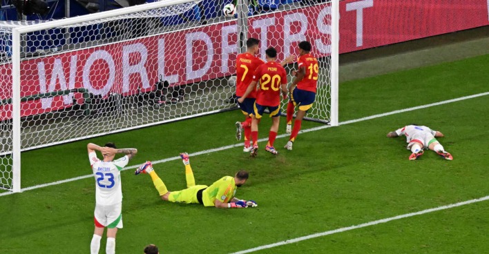 Vor dem Tor eines Fußballfeldes liegen zwei Männer, drei jubeln daneben