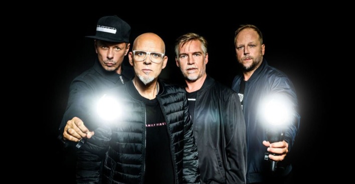 Die Bandmitglieder der "Fantastischen Vier" tragen schwarze Kleidung und blicken ernst in die Kamera. Die zwei Bandmitglieder, die links und rechts stehen, halten auch eine Taschenlampe, die besonders hell leuchtet.