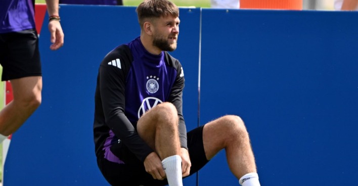 Niclas Füllkrug sitzt am Rasen auf einem Fußball.