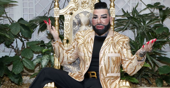 Harald Glööckler mit einer goldenen Jacke auf einem goldenen Stuhl.