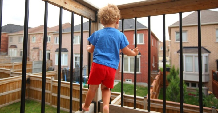 Ein kleiner Bub steht allein auf einem Balkon.