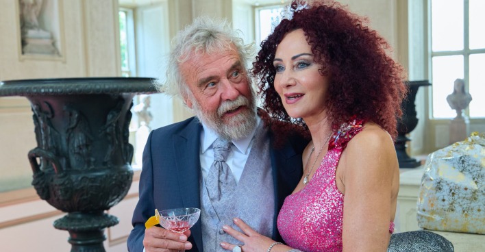 Mausi Lugner und Ernst Prost. Sie trägt ein pinkes Glitzerkleid und er einen blauen Anzug.