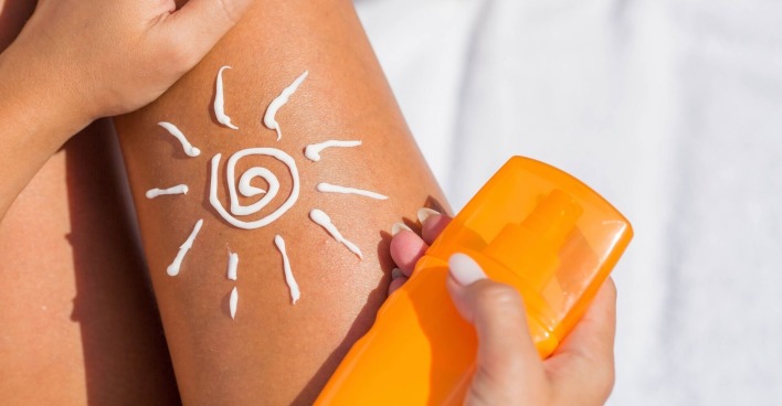 Ein braungebranntes Damenbein, darauf ist aus Sonnencreme eine Sonne gezeichnet, daneben eine Tube Sonnencreme