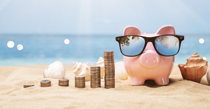 Ein Sparschwein am Strand, daneben Münzstapel
