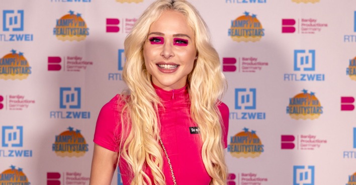 Theresia Fischer mit offenen blonden gewellten Haaren und einem pinken Outfit.