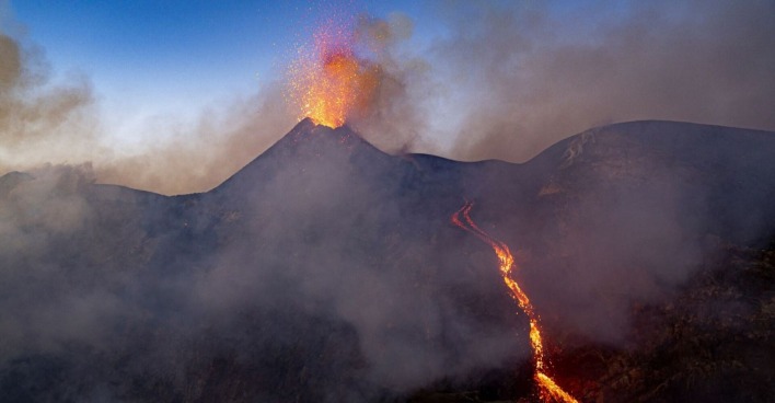 Der Ätna bei Dämmerung spuckt Lava und Rauchwolcken, an der Seite des Vulkan fließt Lava herab