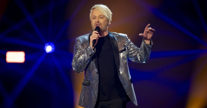 Anthony Ross in einem silber glitzernden Sakko auf der Bühne.
