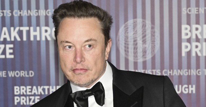 Elon Musk von einer Fotowand im Smoking.