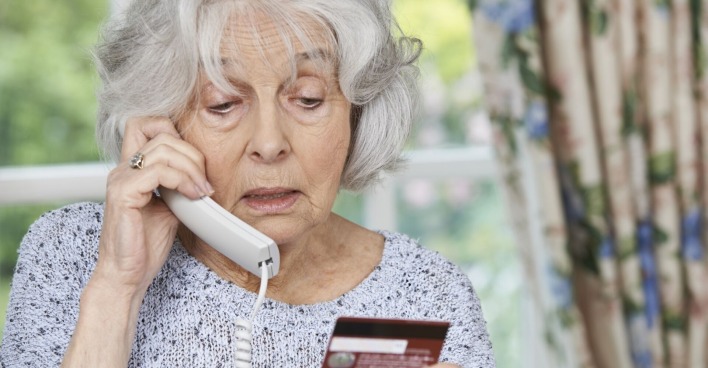 ältere Dame telefoniert und wirft dabei einen Blick auf ihre Kreditkarte